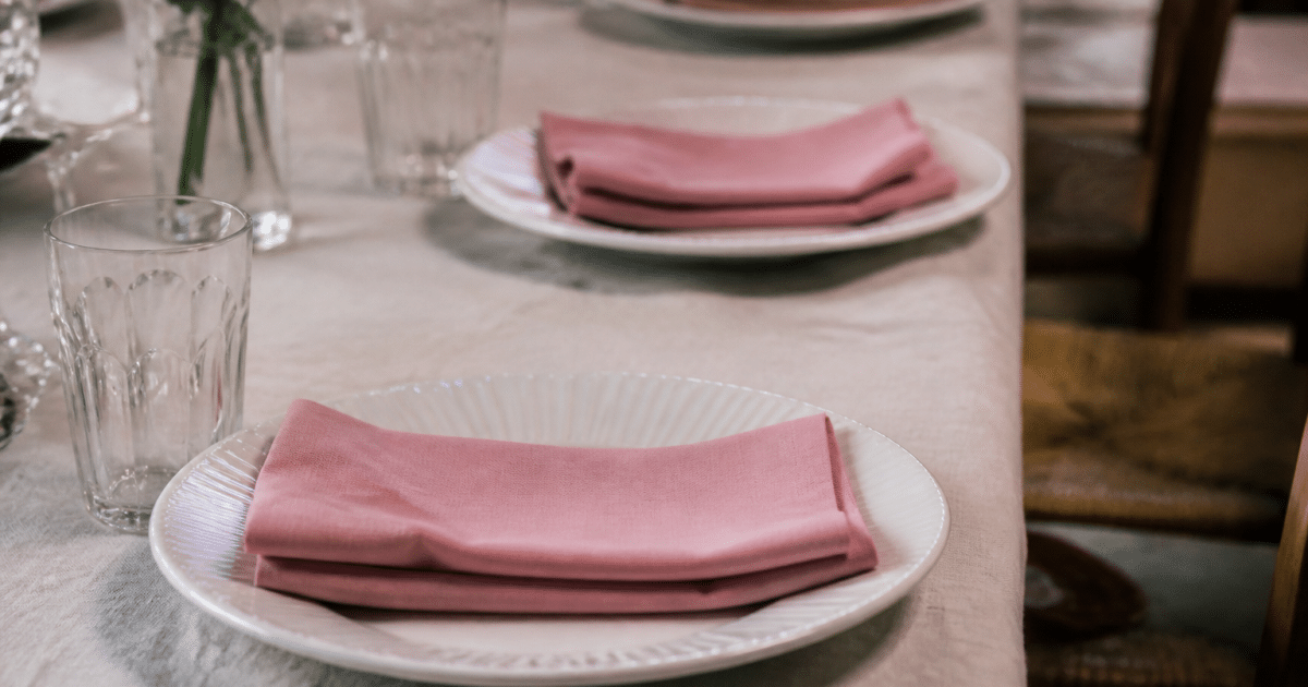 Assiettes blanches alignees avec serviettes roses plies sur nappe claire