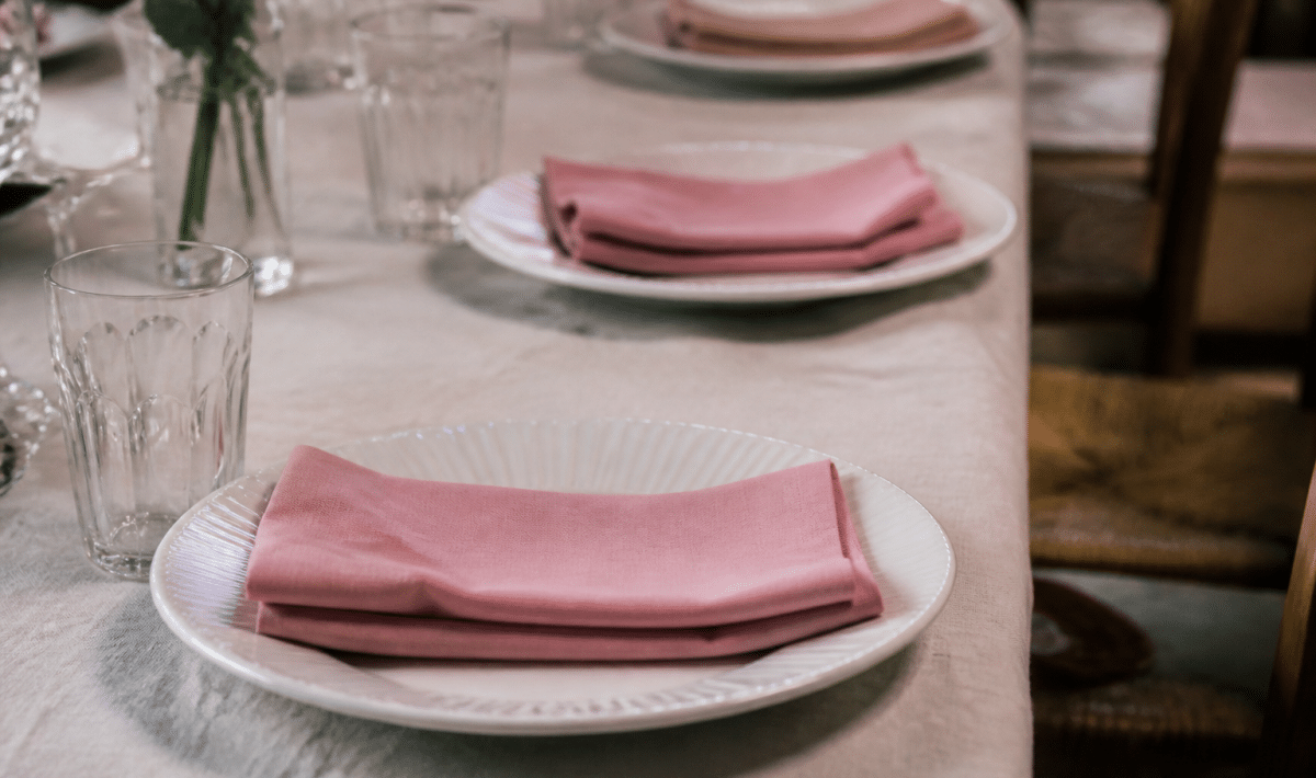 Assiettes blanches alignees avec serviettes roses plies sur nappe claire